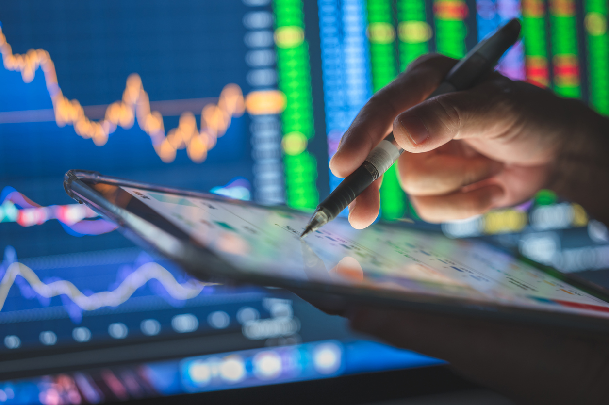 Hand interacting with a digital tablet displaying green and red financial graphs, representing secure data management or coding for trading in secure data management, developing trading algorithms, or cybersecurity oversight in digital systems